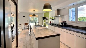 A modern kitchen with a central island, stainless steel appliances, and a large window providing natural light. - Beautiful Villa with Large Heated Pool and Sea Water, 5 km from the Beach (Portiragnes)