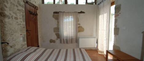 A bedroom with a bed, wooden bench, stone walls, and large windows.