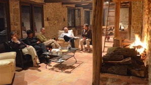 A cozy room with stone walls, wooden beams, and a fireplace. There are several people seated around a coffee table.