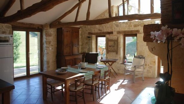 A rustic dining area with exposed wooden beams, stone walls, and a large window providing natural light.