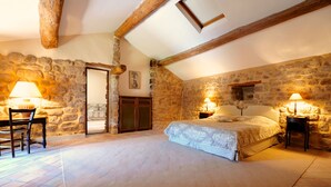 Ein Schlafzimmer mit Stehwänden, einem Bett mit gemustertem Überwurf, zwei Nachttischen mit Lampen und einem Holzstuhl.