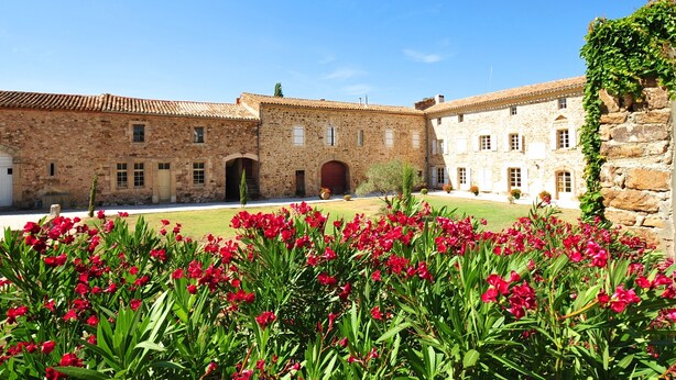 Ein Innenhof mit Steingebäuden, einem zentralen Bogen und roten Blumen im Vordergrund.
