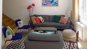 A modern living room with a gray sofa, blue chairs, a coffee table, and a painting of swimmers.