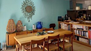 A dining area with a wooden table and chairs, a blue wall, a decorative mirror, and a bookshelf filled with books.