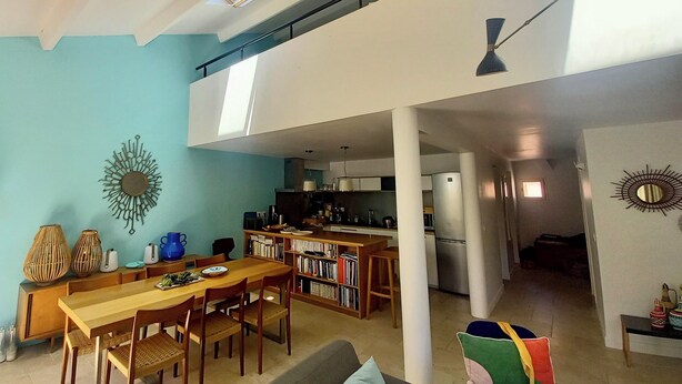 A spacious living area with a dining table, sofa, and a kitchen in the background.