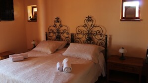 Een keurig opgemaakt bed met opgerolde handdoeken, een nachtkastje met een lamp, en een kleine spiegel aan de muur.