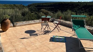 Een terras met uitzicht op zee, een tafel, twee stoelen en een ligstoel.