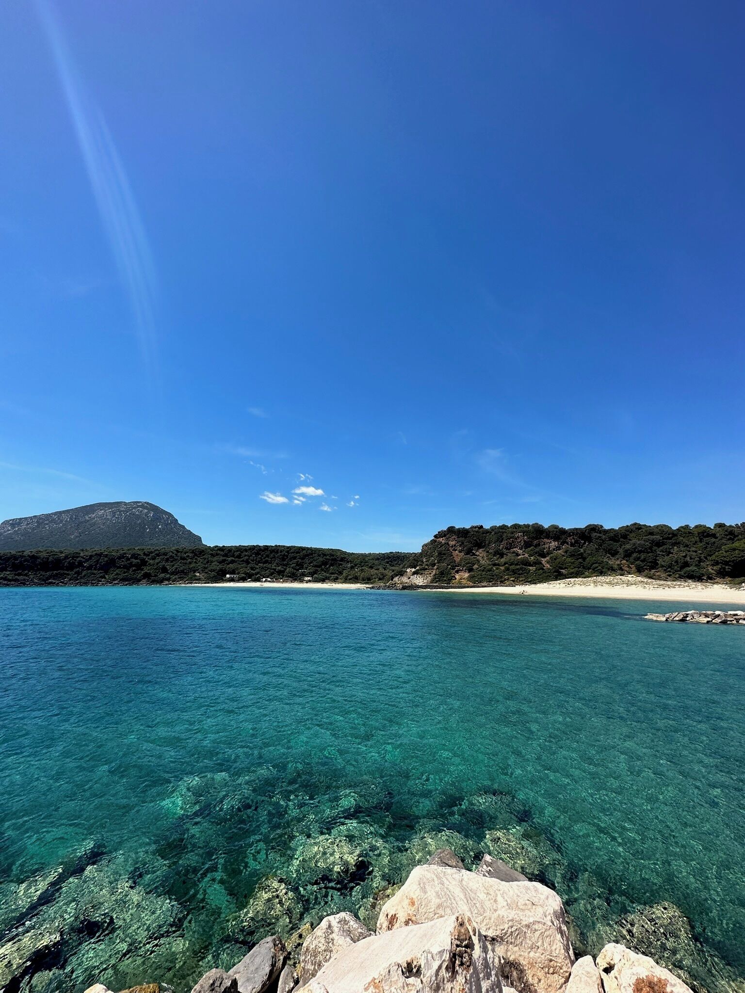 Vista despejada de un paisaje costero con montaña, playa y costa rocosa.