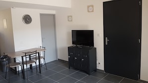 A modern apartment with a dining area, a black cabinet with a flat-screen TV, and a black door.