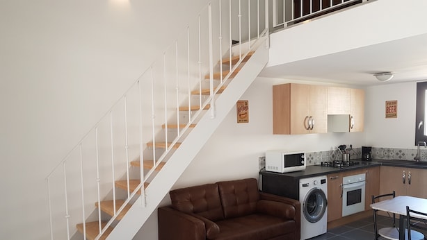 A modern apartment with a staircase, a brown leather sofa, a washing machine, a microwave, and a dining area.