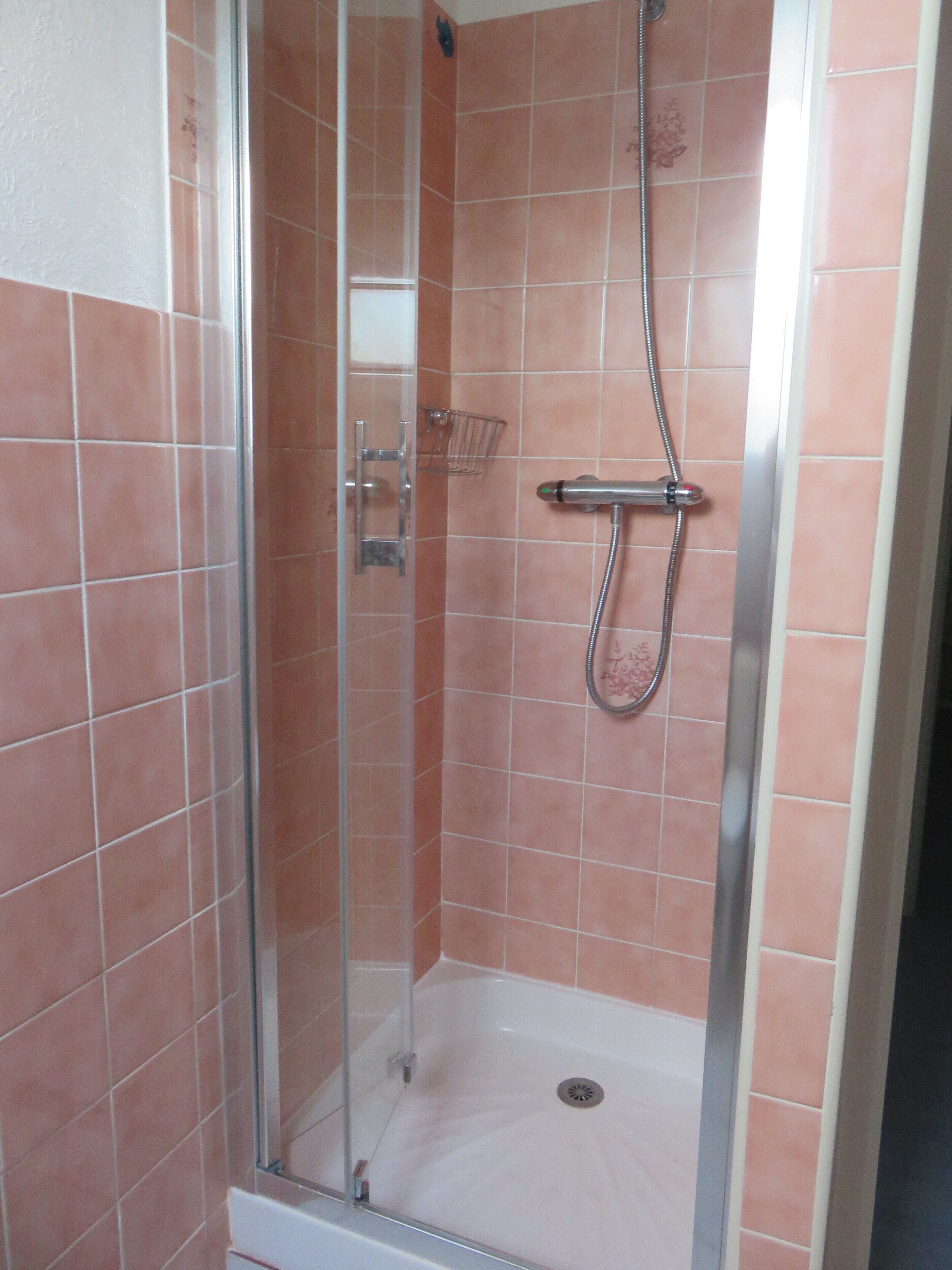 A glass-enclosed shower stall with a handheld showerhead and a wall-mounted faucet.