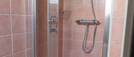 A glass-enclosed shower stall with a handheld showerhead and a wall-mounted faucet.