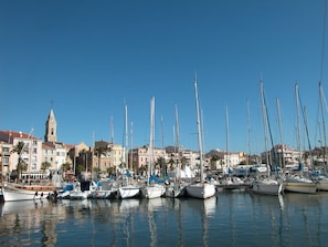 Un port de plaisance où sont amarrés de nombreux voiliers, un clocher d’église imposant et, au loin, des immeubles d’habitation.