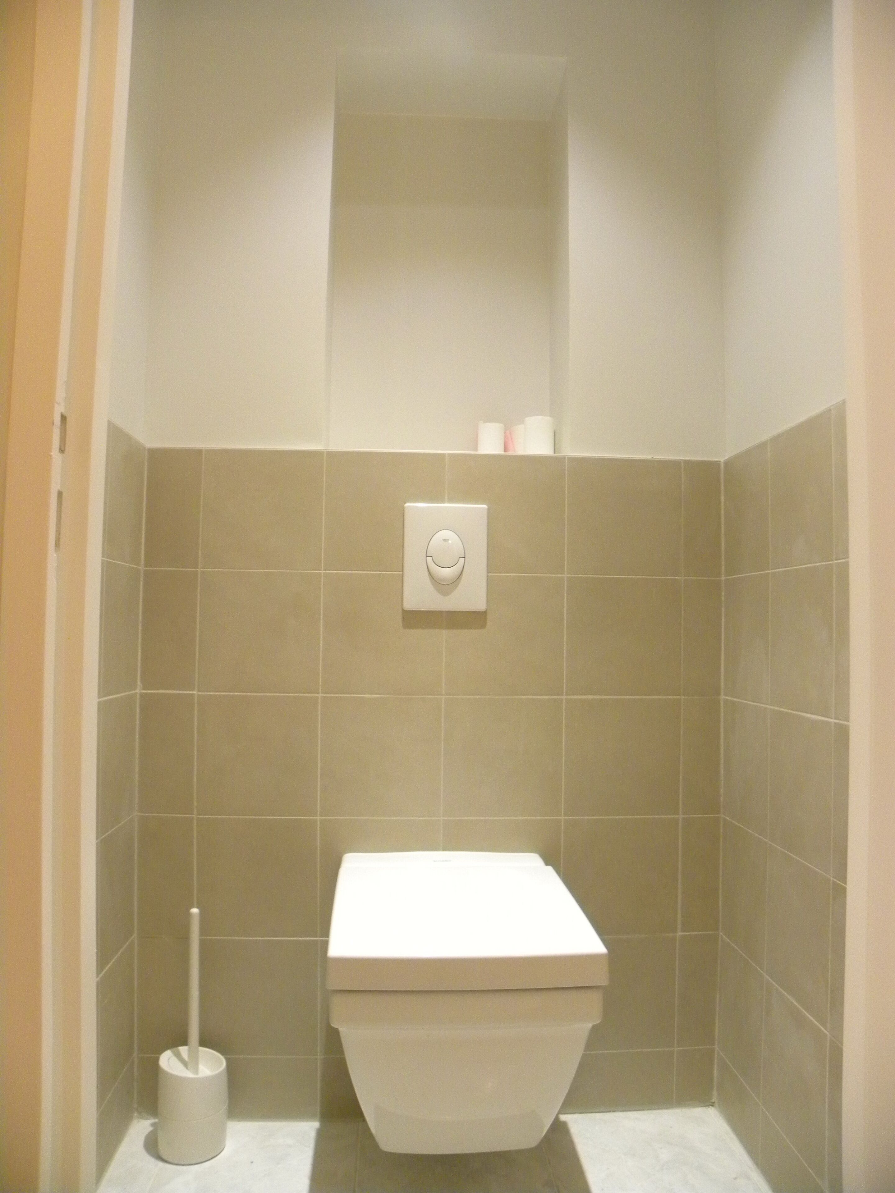 Un baño pequeño y limpio con inodoro, escobilla y pulsador en la pared.