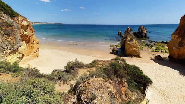 Un paisaje costero con una playa arenosa, formaciones rocosas y aguas azules cristalinas.