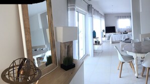 Un comedor moderno con una mesa grande y sillas blancas, un televisor al fondo y vistas al salón.
