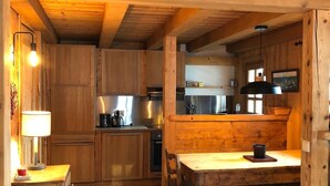 Interior em madeira com cozinha, armários, mesa de jantar com cadeiras e um banco.