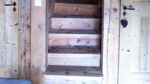 Escada de madeira que leva a um andar superior, com portas de madeira e maçanetas de metal ao lado.