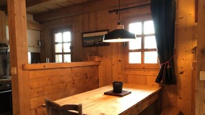 Interior de madeira com mesa de jantar, cadeiras, um banco e luminária pendente.