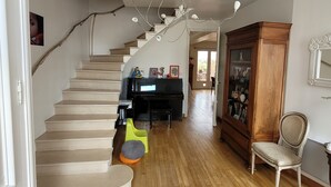 Een ruime woonkamer met een houten trap, een kroonluchter, een piano en een grote houten kast.