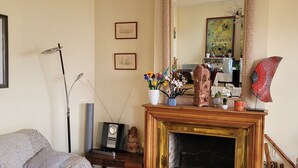 Een woonkamer met een bank, een glazen salontafel, een open haard, een spiegel en ingelijste foto's aan de muur.