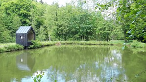 A small, dark-colored birdhouse by a calm pond surrounded by lush greenery. - Charming cottage classified 3 stars in an old renovated mill. Comfort. (Schoenbourg)