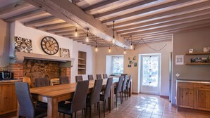 A spacious dining area with a long wooden table and multiple chairs, a stone fireplace, and exposed wooden beams on the ceiling.