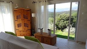 Une chambre à coucher avec un lit, une armoire en bois et une vue sur un paysage verdoyant, visible à travers une porte-fenêtre coulissante.