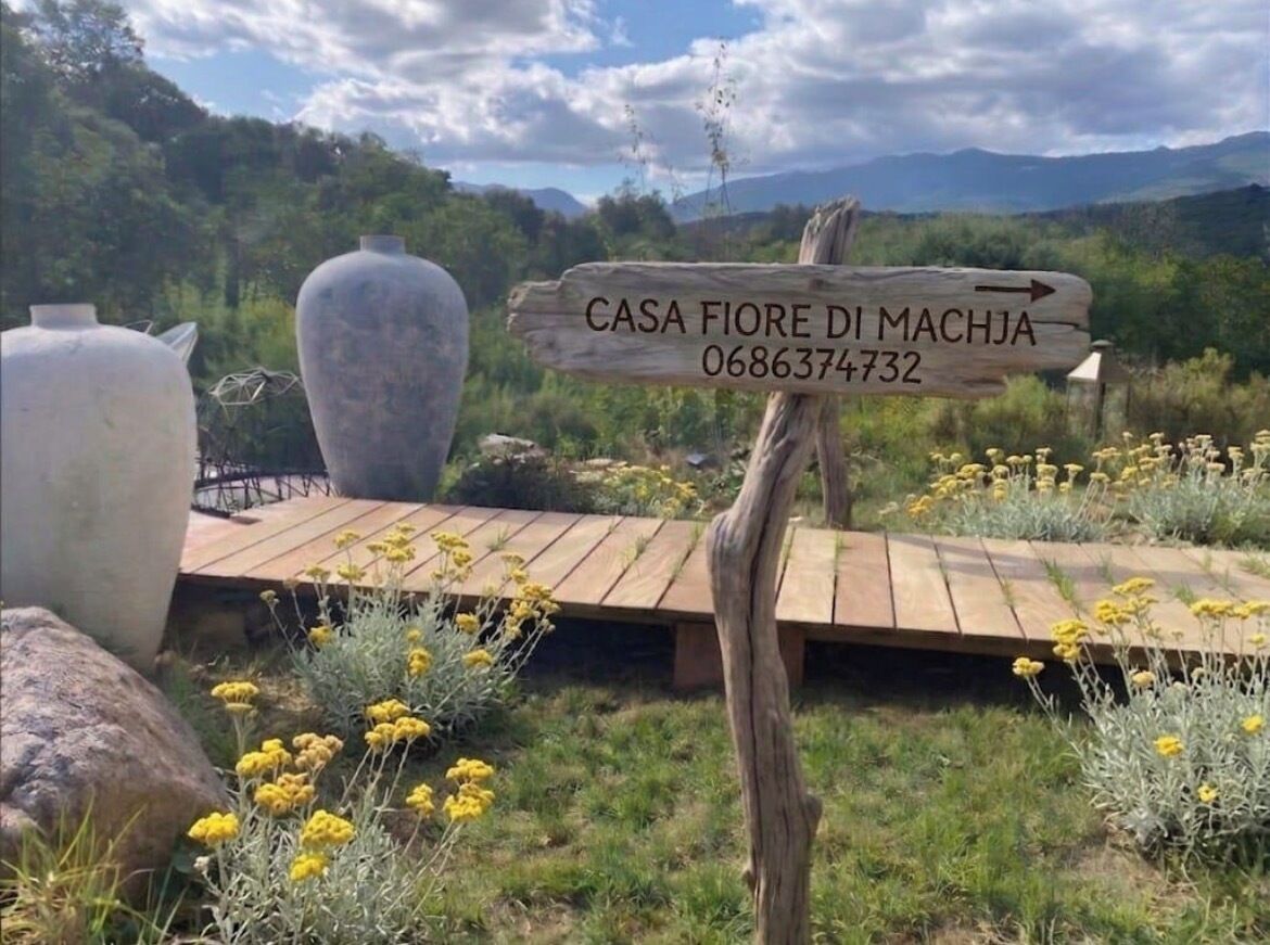Un panneau indicateur en bois portant l’inscription « CASA FIORE DI MACHJA 0686374732 » et pointant vers la droite.