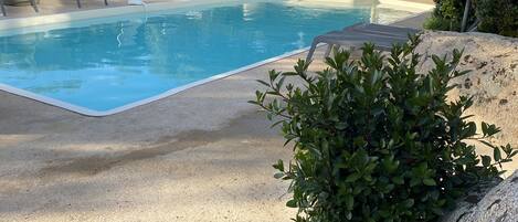 A swimming pool with lounge chairs and a covered seating area.