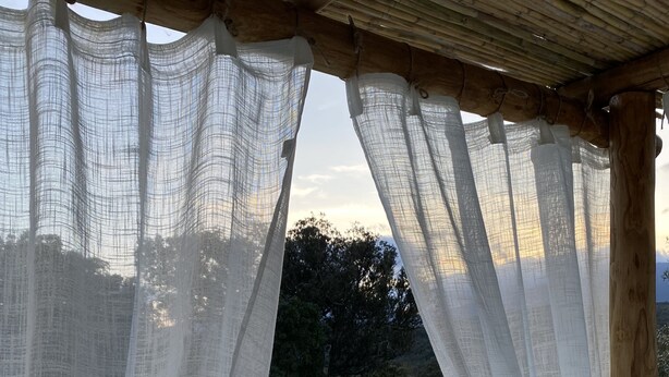 Un espace piscine agrémenté d’une pergola en bois et de rideaux blancs.