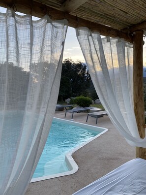 Uma área de piscina com pergolado de madeira e cortinas brancas.