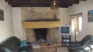 Een woonkamer met een stenen open haard, leren banken, een televisie en een houten salontafel.