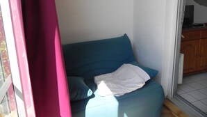A room with a blue sofa, a white pillow, and a pink curtain. - pleasant studio for spa guests (Balaruc-Les-Bains)