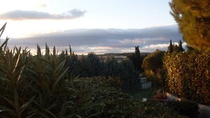 A garden with various plants and trees, a clear sky, and distant hills. - pleasant studio for spa guests (Balaruc-Les-Bains)