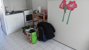 A kitchen with white cabinets, a stove, and a sink. There is a green bag with fruit images on the floor. - pleasant studio for spa guests (Balaruc-Les-Bains)