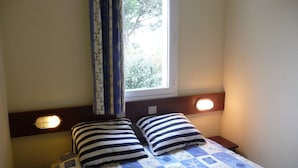 A bed with striped pillows, a quilt with nautical patterns, a window with curtains, and wall-mounted reading lights. - 2 roomed apartment for 4 to 5pers, ground garden, stunning sea views, à150m Beach (Arzon)