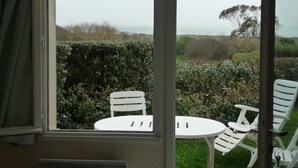 A room with a window overlooking a garden with white chairs and a table. - 2 roomed apartment for 4 to 5pers, ground garden, stunning sea views, à150m Beach (Arzon)