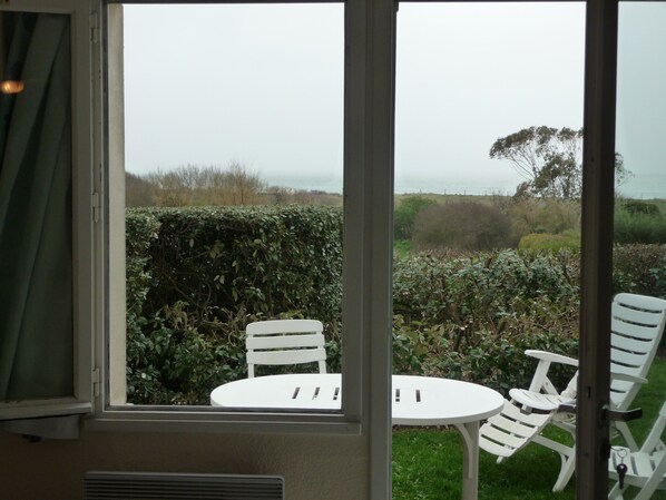 A room with a window overlooking a garden with white chairs and a table.