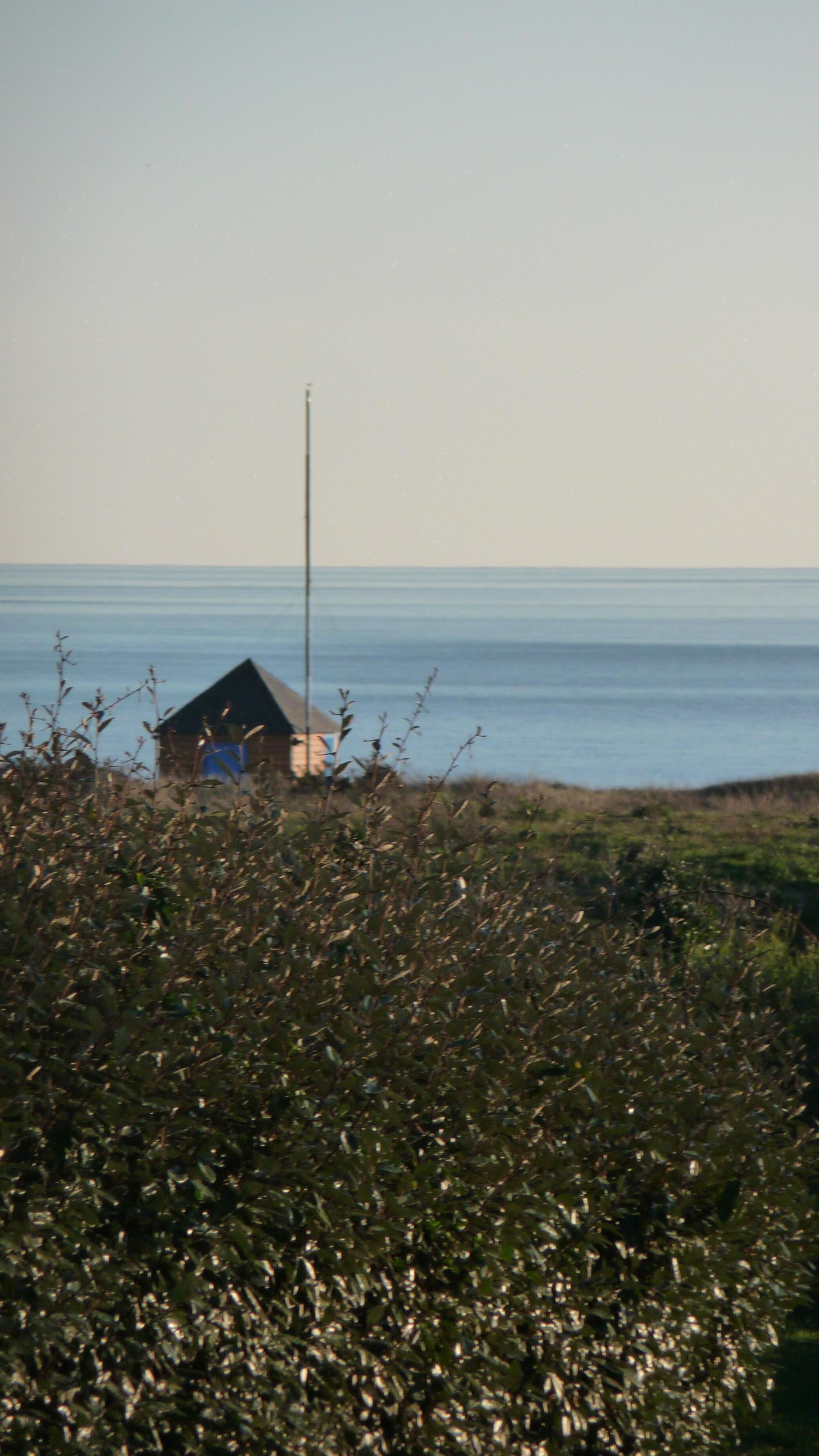 Un paysage côtier avec un petit bâtiment et un grand poteau.