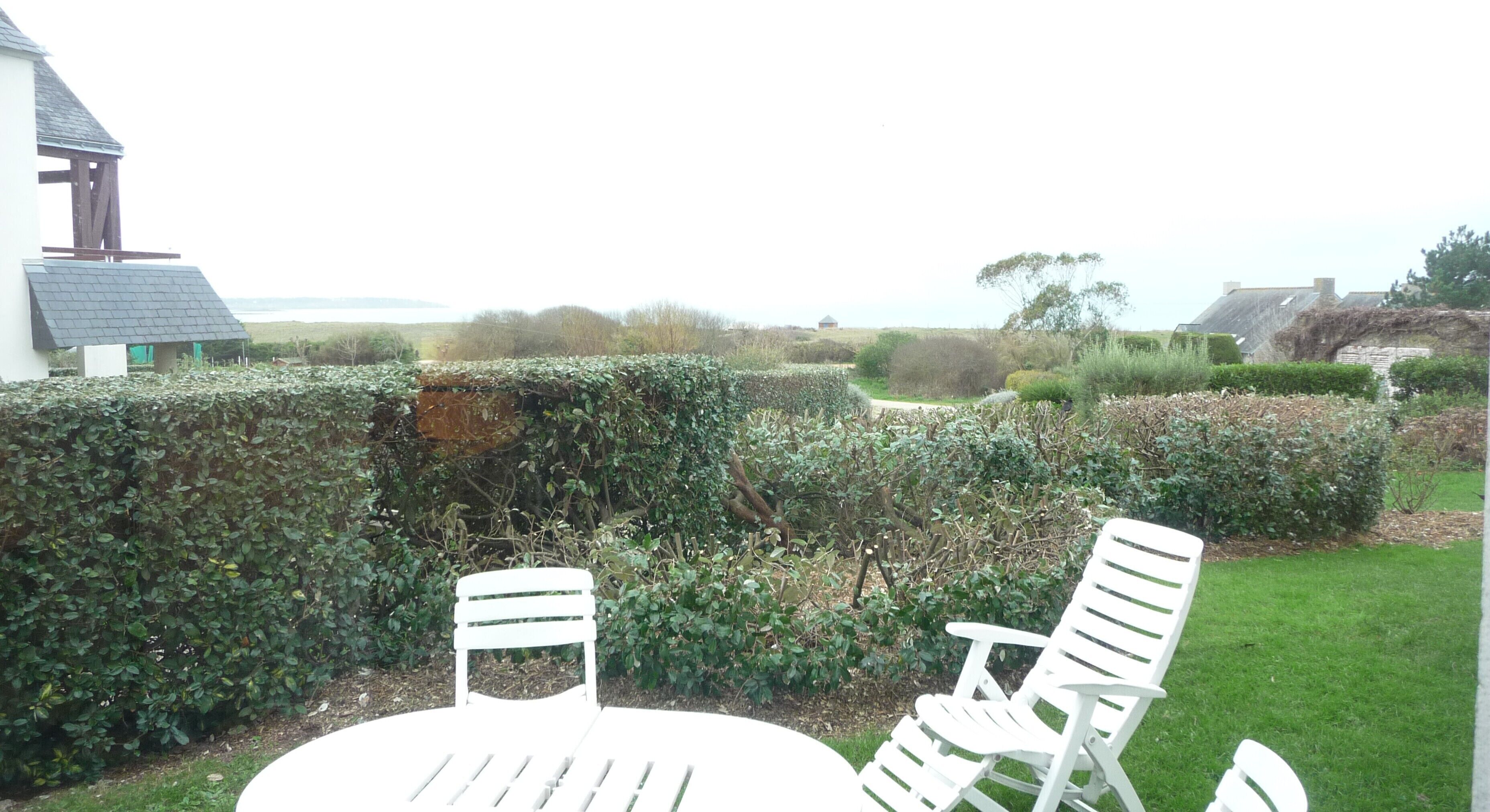 A garden with a round table and four white chairs.