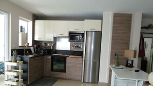 A modern kitchen with stainless steel appliances, a microwave, and a refrigerator. There is a small dining area with a table and chairs.