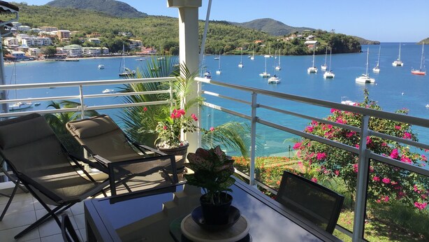 A balcony with a table, chairs, and potted plants overlooking a marina with boats.