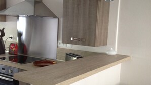 Une cuisine moderne dotée d’une hotte en acier inoxydable, d’un four encastré, d’un grille-pain et d’un plan de travail en bois. On y trouve deux tabourets de bar noirs et un luminaire suspendu.
