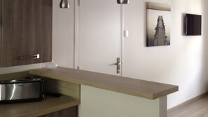 Une cuisine moderne avec des armoires en bois, un four à micro-ondes encastré, des luminaires suspendus, une porte et un tableau encadré au mur.