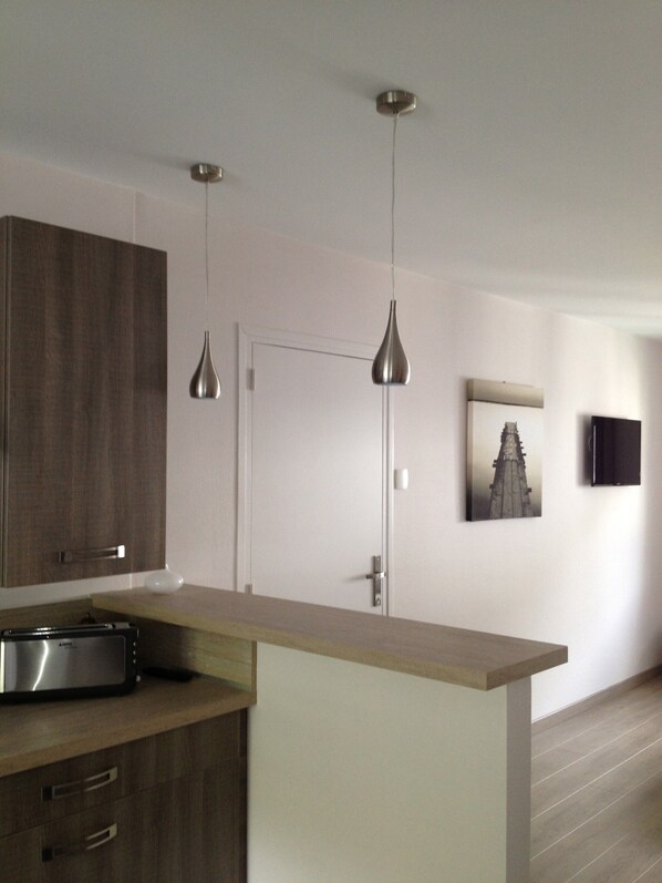 Une cuisine moderne avec des armoires en bois, un four à micro-ondes encastré, des luminaires suspendus, une porte et un tableau encadré au mur.
