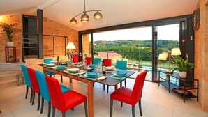 A dining area with a large table set for six, surrounded by red and blue chairs, with a view of a pool and greenery outside. - Charming house with private pool near Sarlat in beautiful grounds (Sarlat-La-Canéda)