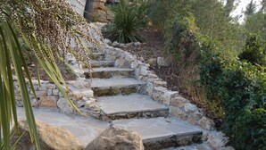 Eine steinerne Treppe führt einen Hügel hinauf, umgeben von Grün und Steinen.