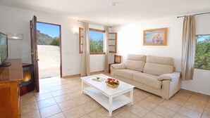 A living room with a sofa, a coffee table with a book and flowers, a TV, and a door leading outside. - Villa José 1, 12 Pers, Sea View ! Heated pool,  Wifi,A/C, petfriendly (Comares)