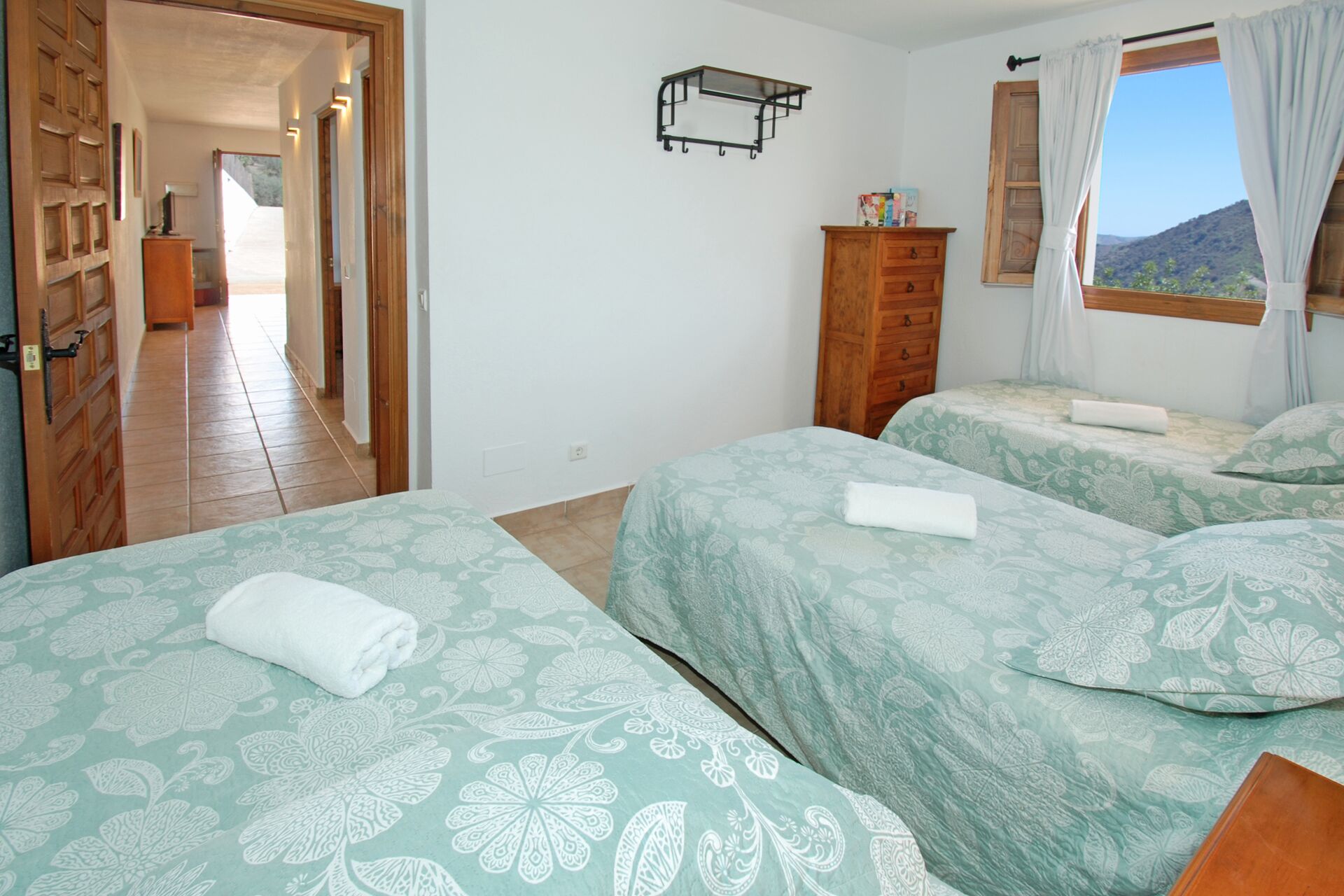 A bedroom with two beds, a wooden wardrobe, a small table, and a window with curtains.